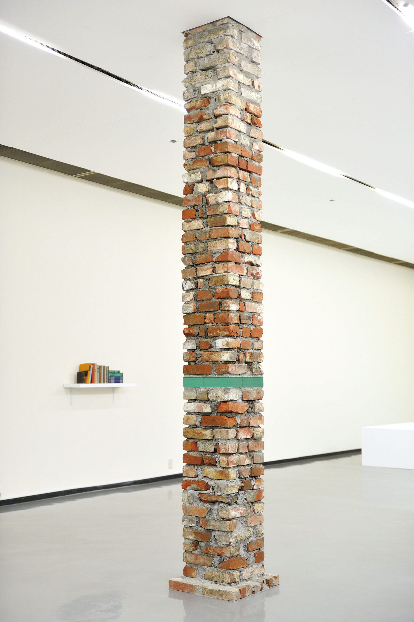 a tall sack of bricks stands in a gallery, including an embedded section of layered of aquamarine glass