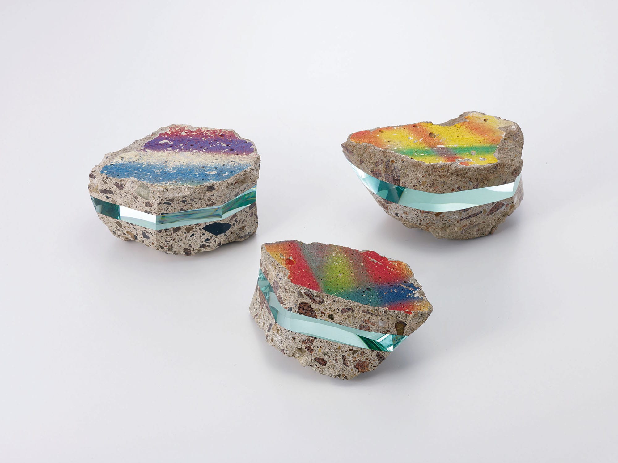 three painted rocks, each include an embedded section of layered of aquamarine glass