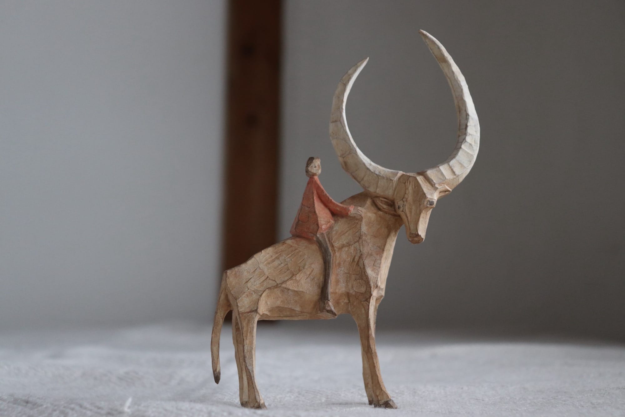 a wooden sculpture of a small figure on the back of a long-horned cow