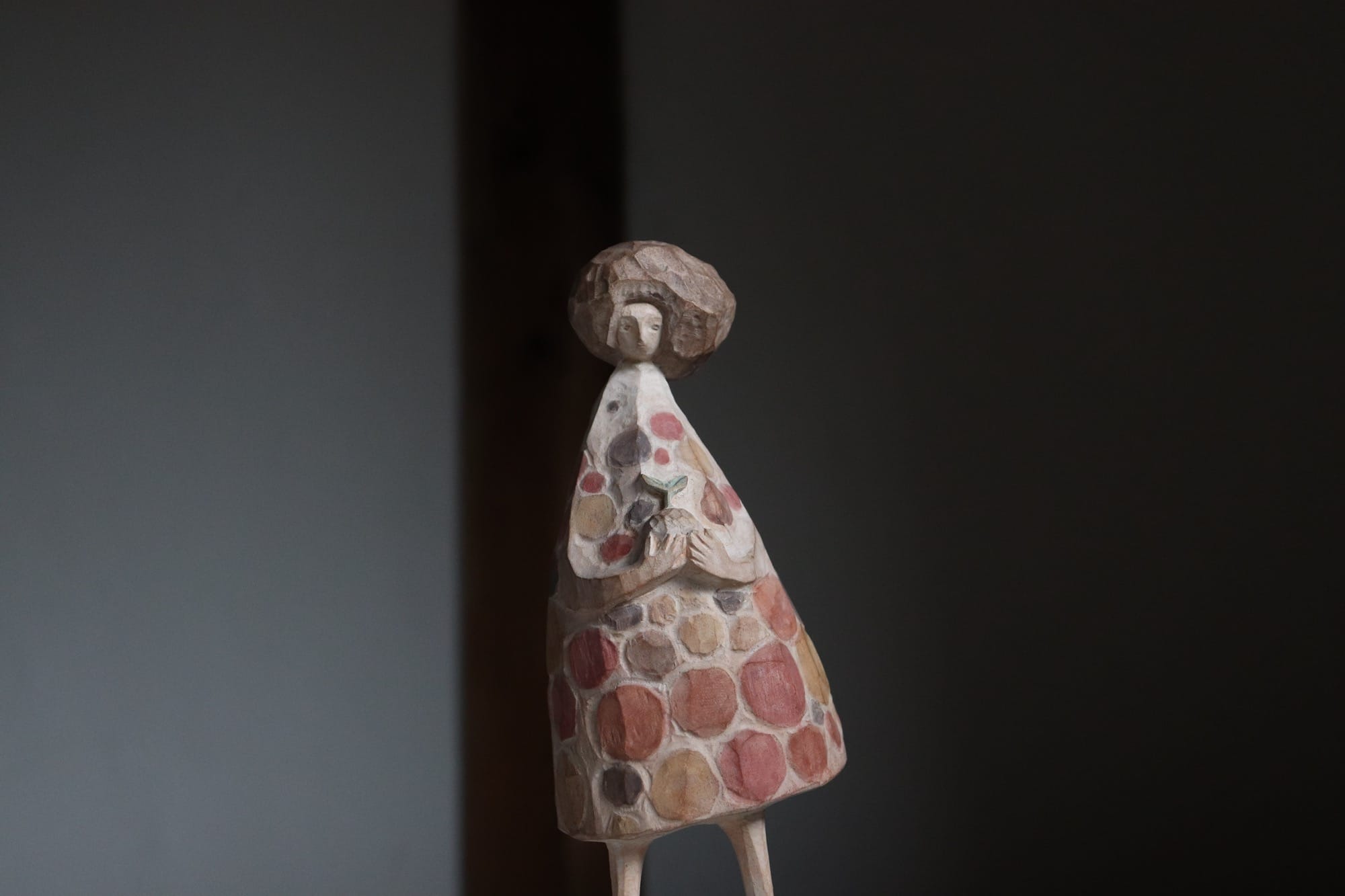 a wooden sculpture of a figure wearing a colorful dotted dress, with hair that appears to be blowing in the wind