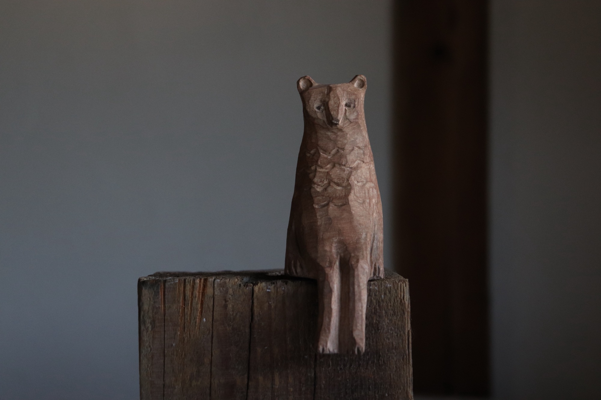 a wooden sculpture of a bear-like creature sitting on another piece of unworked timber