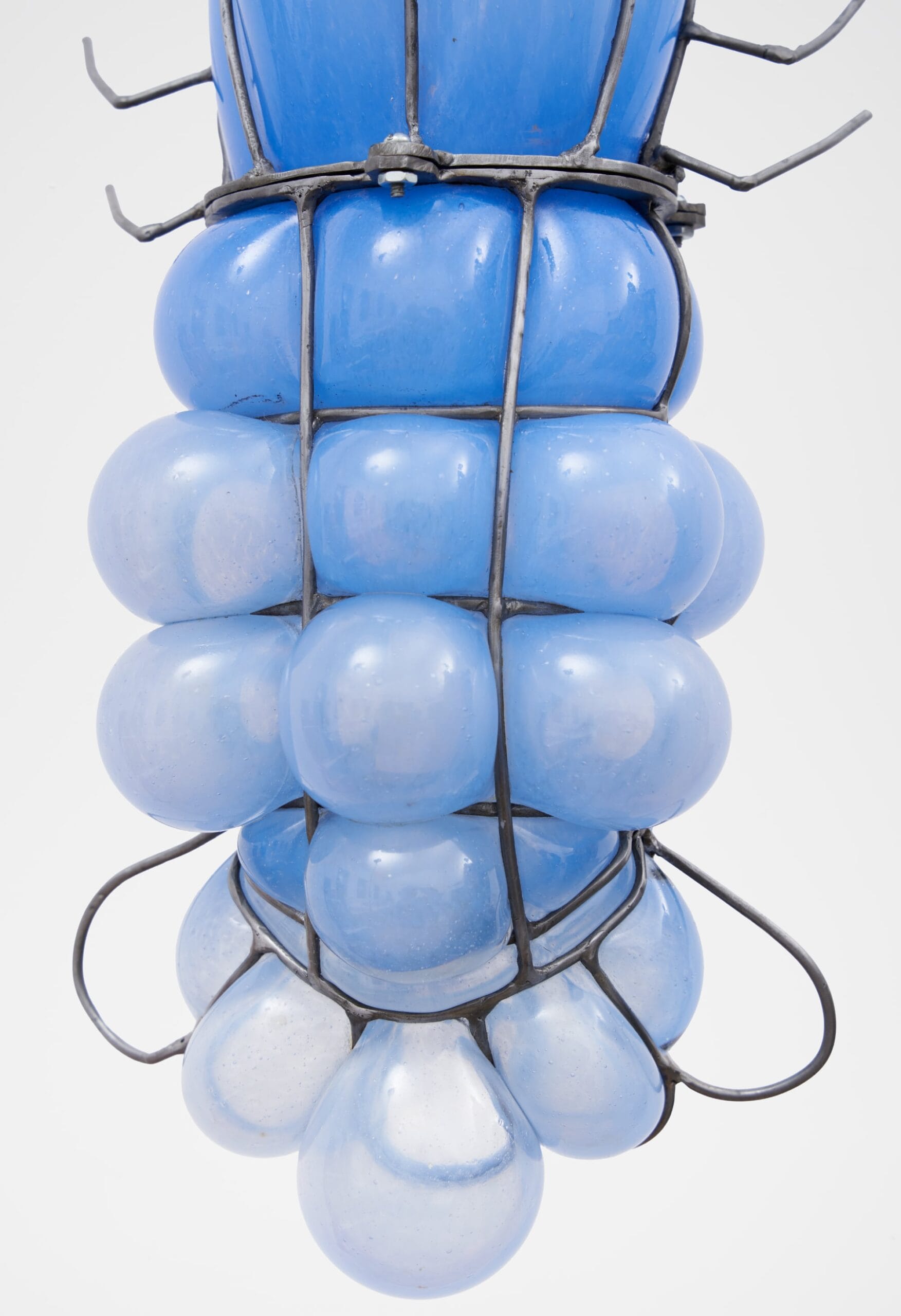 a close up image of the bottom of a glass blown pendant lamp that bubbles inside steel armature and appears like a blue lobster