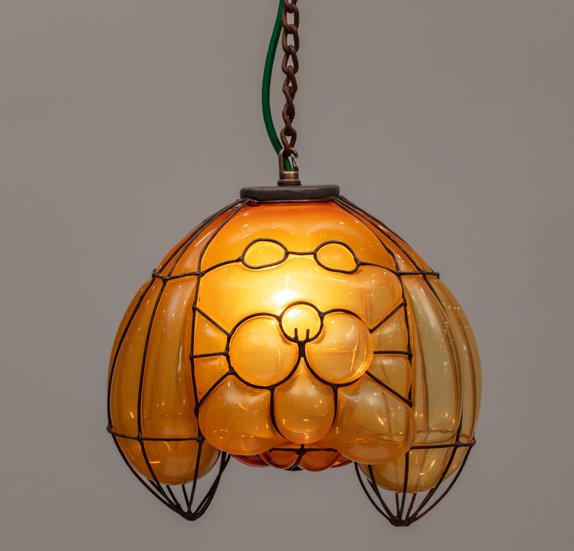a glass blown pendant lamp hanging from a chain that bubbles inside steel armature and appears like a yellow insect
