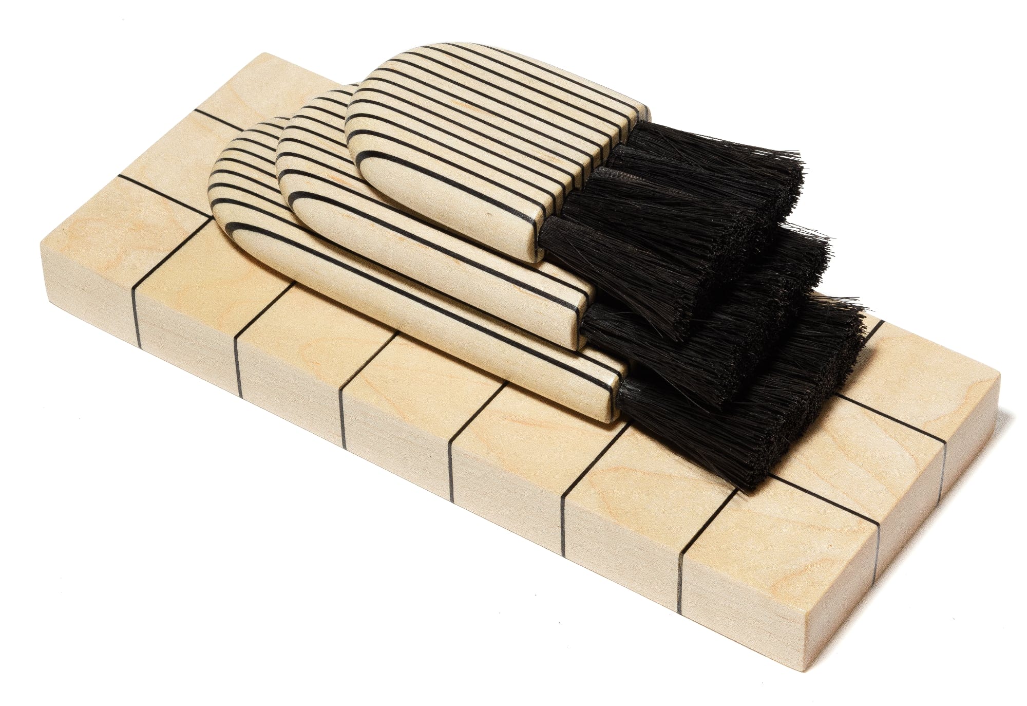 a stack of three black striped wooden brushes with a black brush on a gridded piece of wood