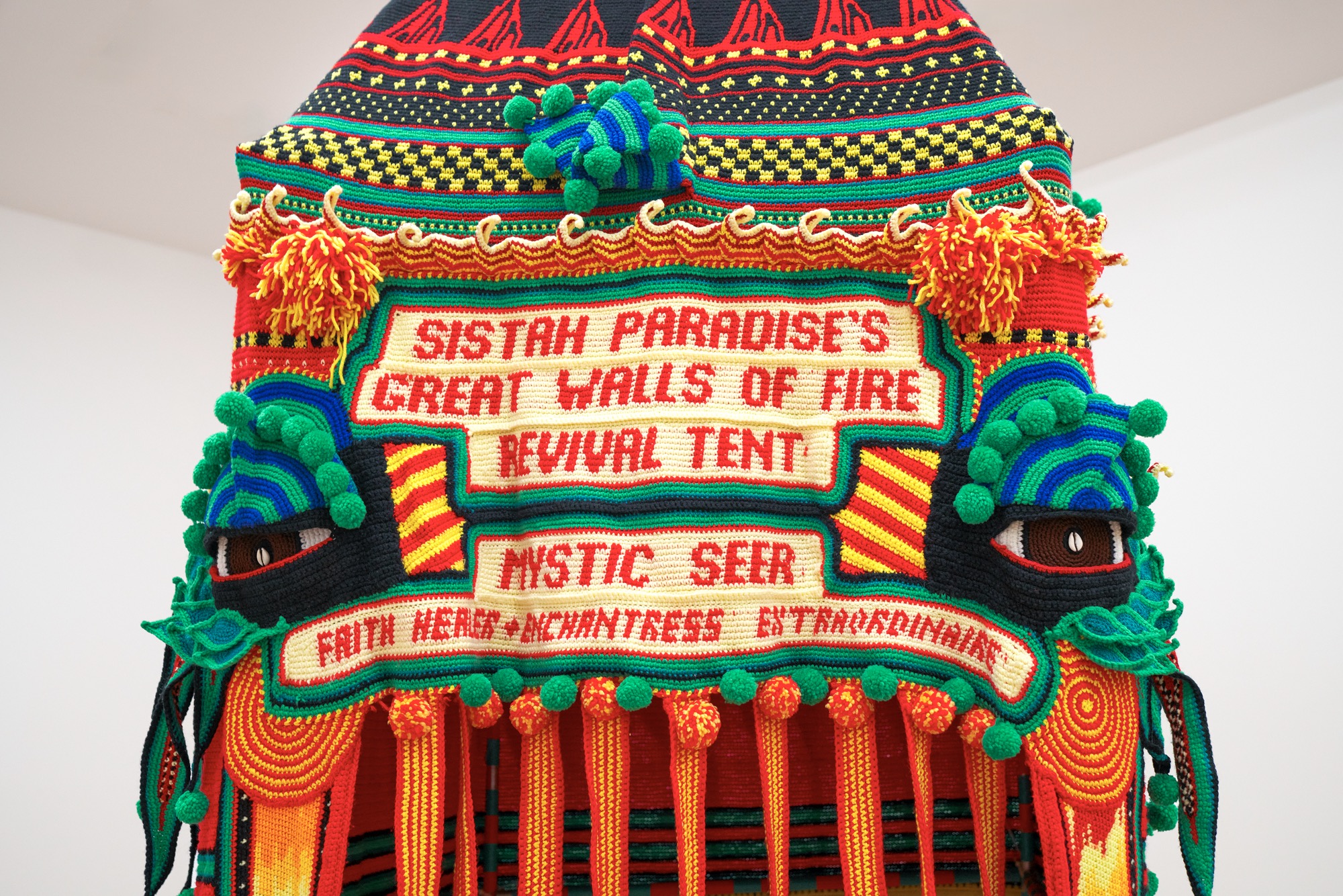 detail of a crocheted artwork shaped like a tent with the phrase "sistah paradise's great walls of fire revival tent—mystic seer"
