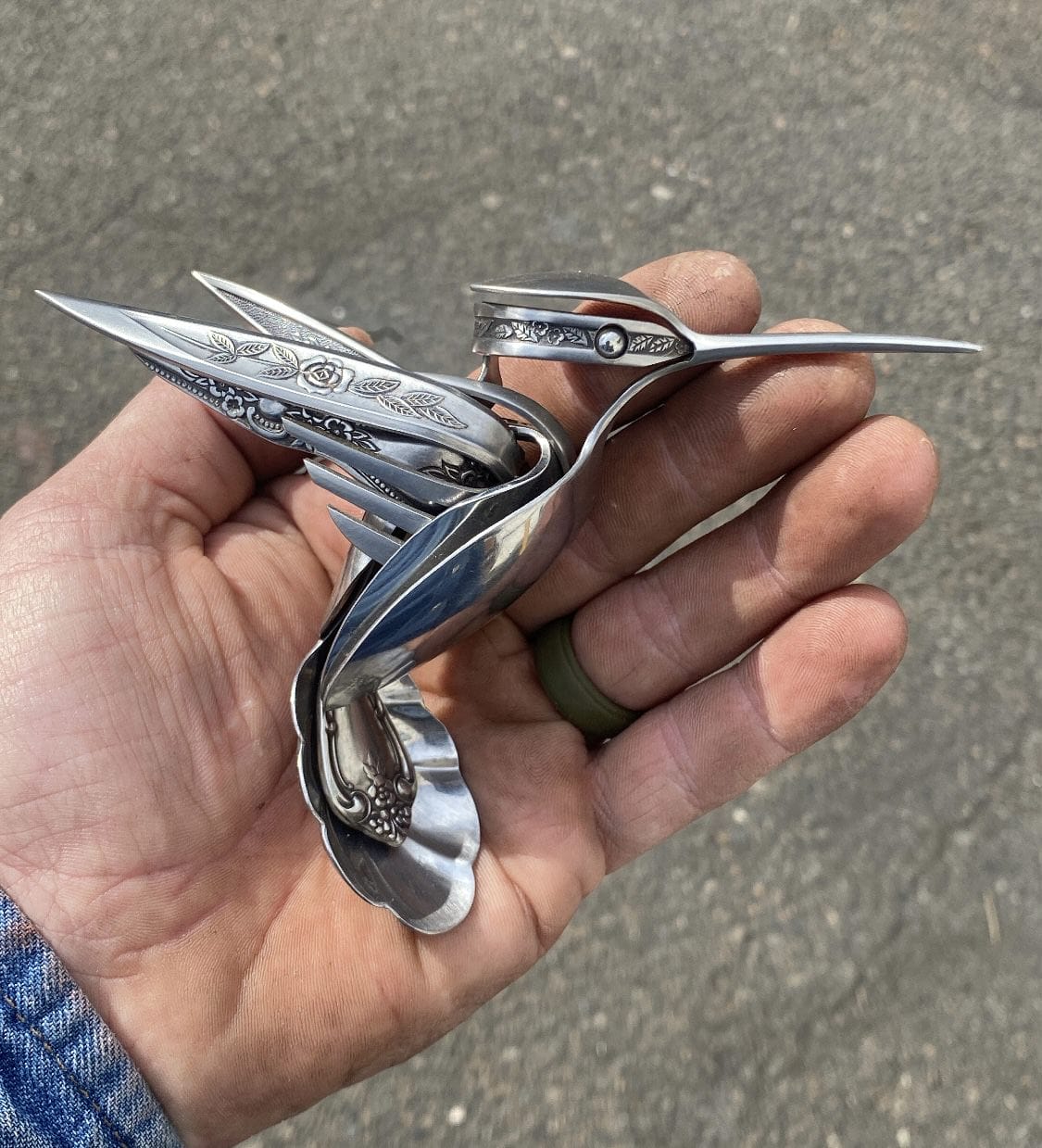 a hand holds a small metal bird made from repurposed silverware