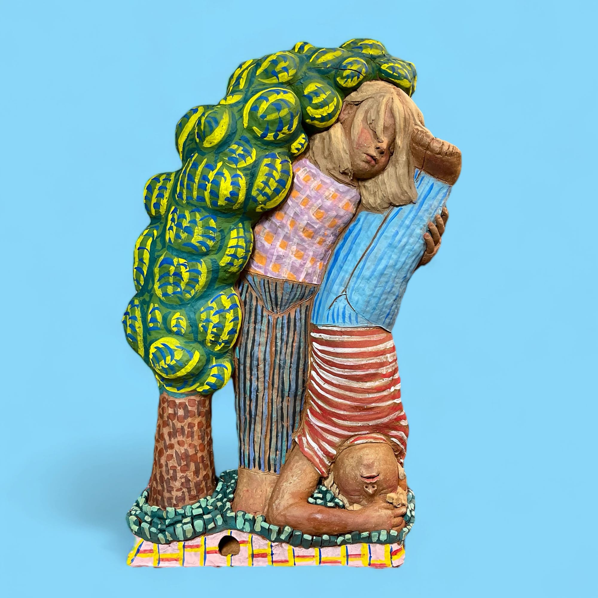 a ceramic sculpture of two children leaning on each other. a tree to their right leans on them as well.