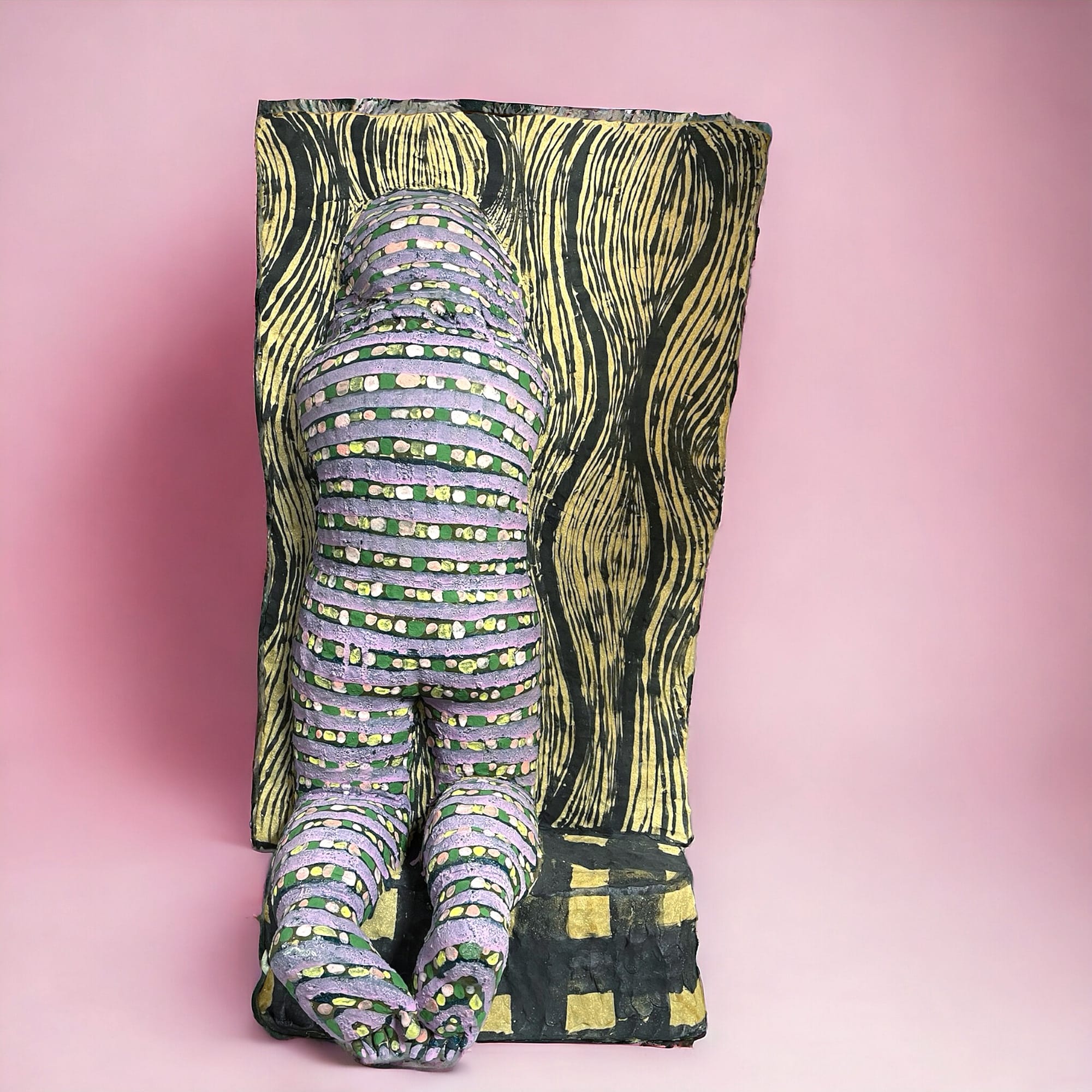 a ceramic sculpture of the back of a patterned figure kneeling. the figure disappears into a patterned background