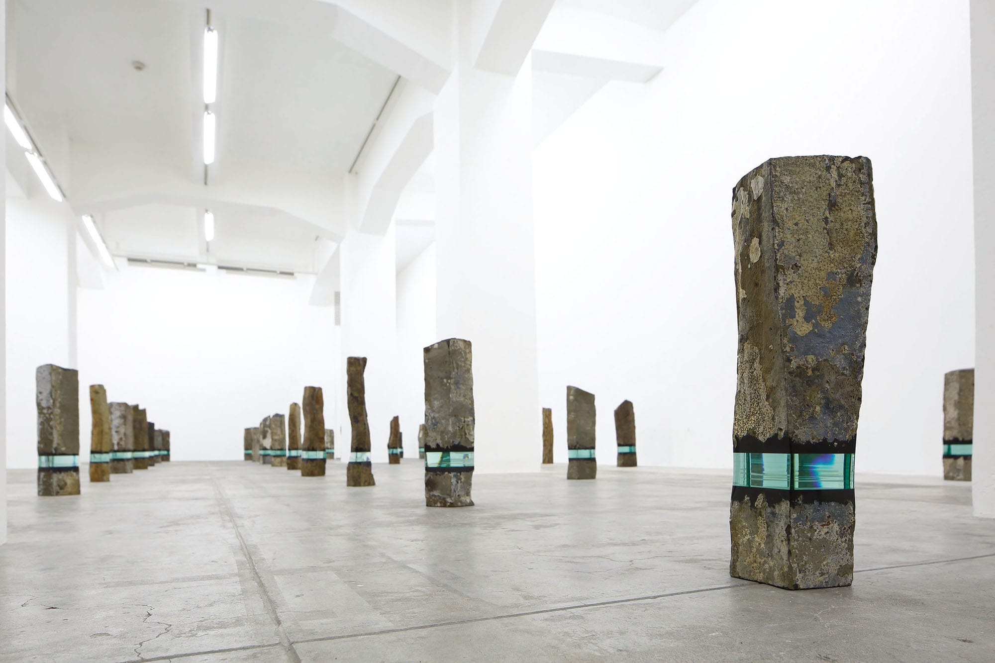 tall pillars of basalt stand in a gallery, each including an embedded section of layered of aquamarine glass