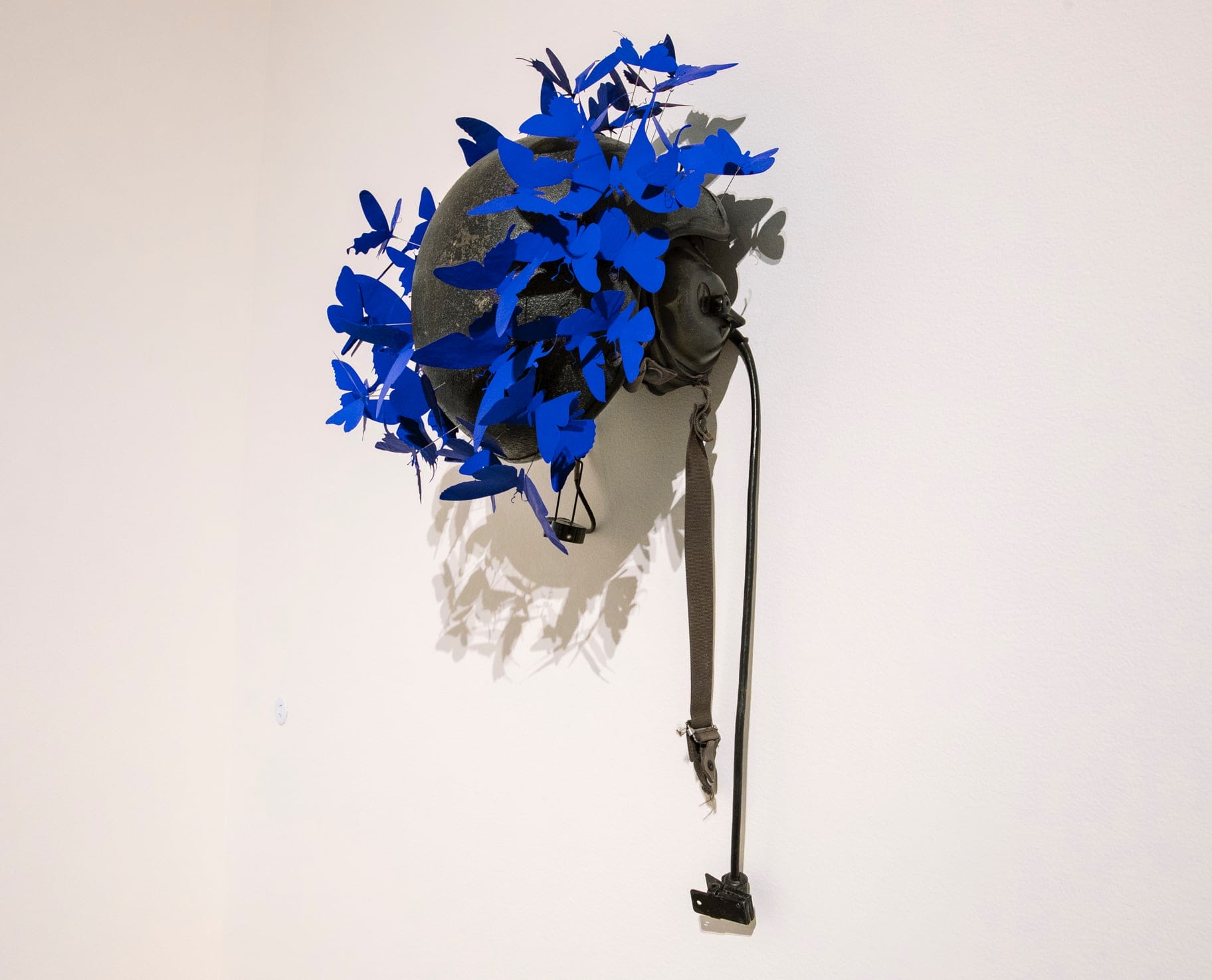 a wall sculpture of a pilot's helmet swarmed with bright blue butterflies made from aluminum
