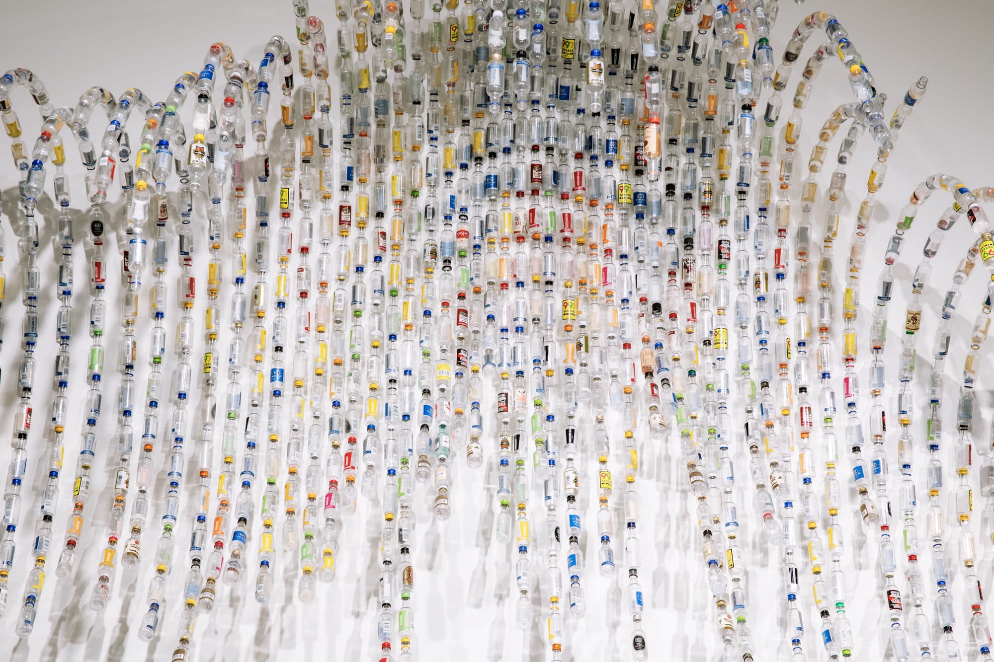 a detail of a wall sculpture that resembles the rhythms of a starling murmuration, made from tiny liquor bottles