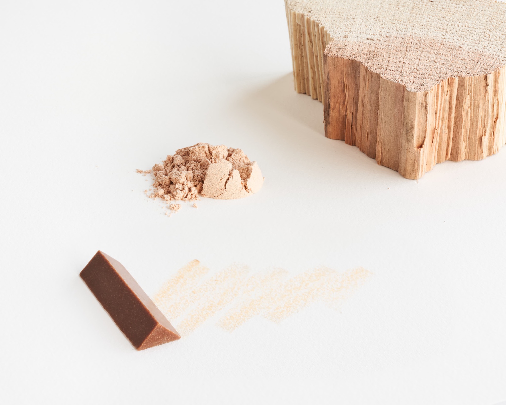a triangular crayon with a warm rusty hue, shown next to a piece of timber from which its pigment was ground